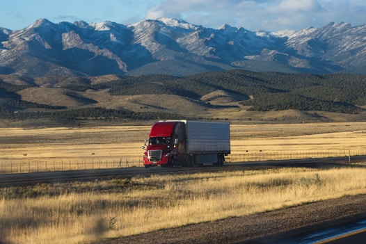 A red semi truck driving down a rural road