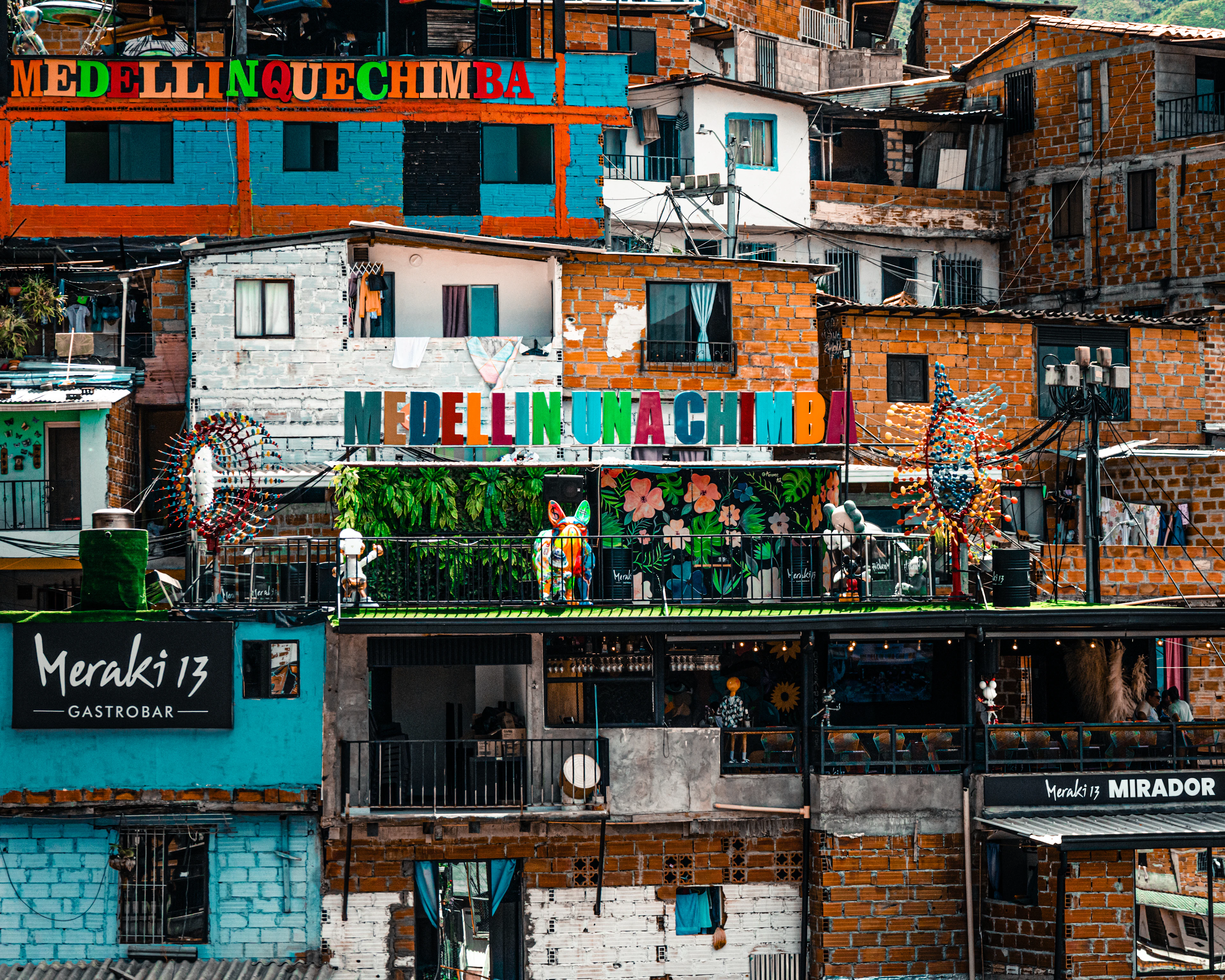 Stacked painted houses, murals reading MEDELLIN and hillside terrace bars in the Comuna 13 neighbourhood