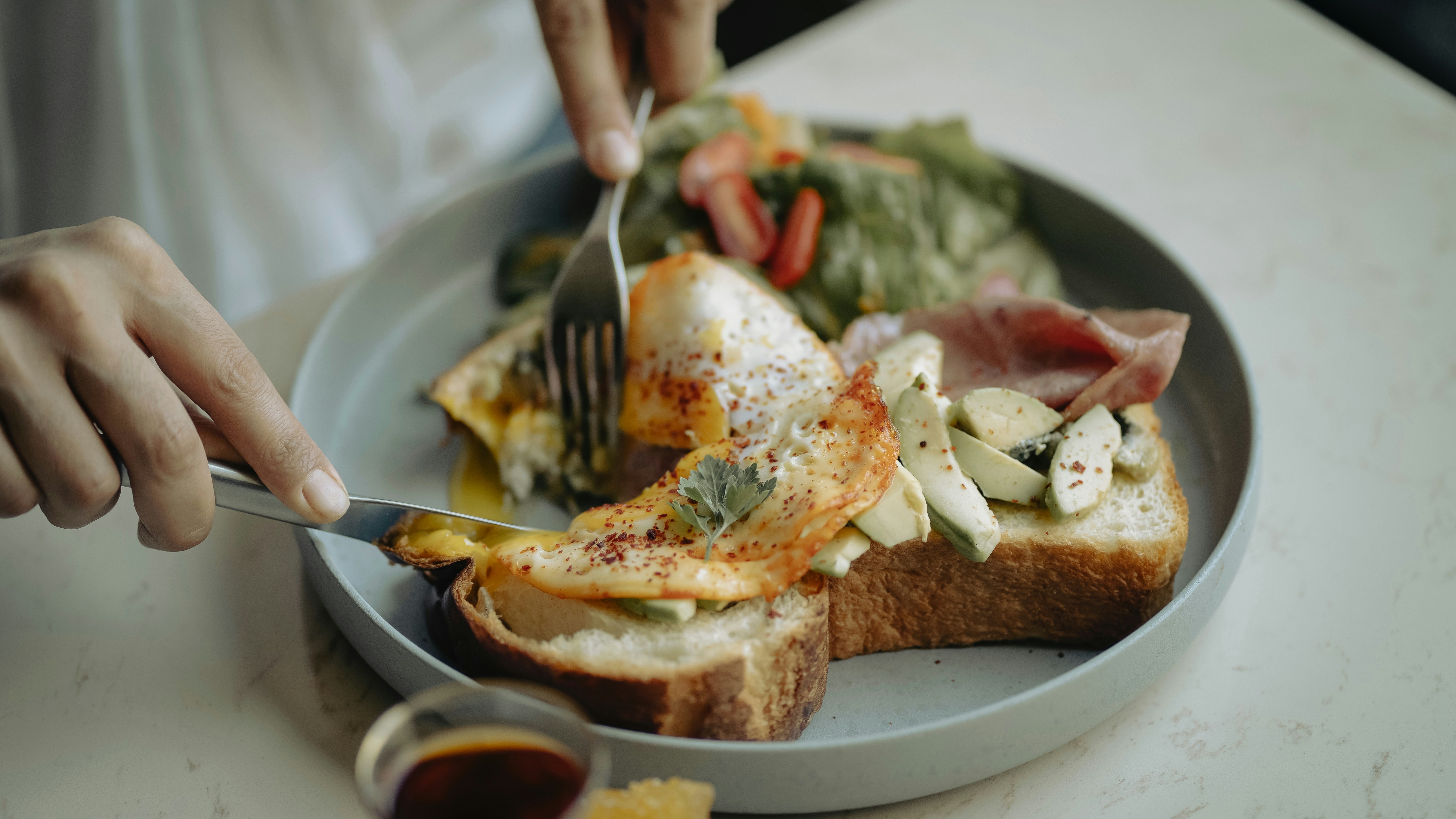 A person cutting into a sandwich with a knife and fork