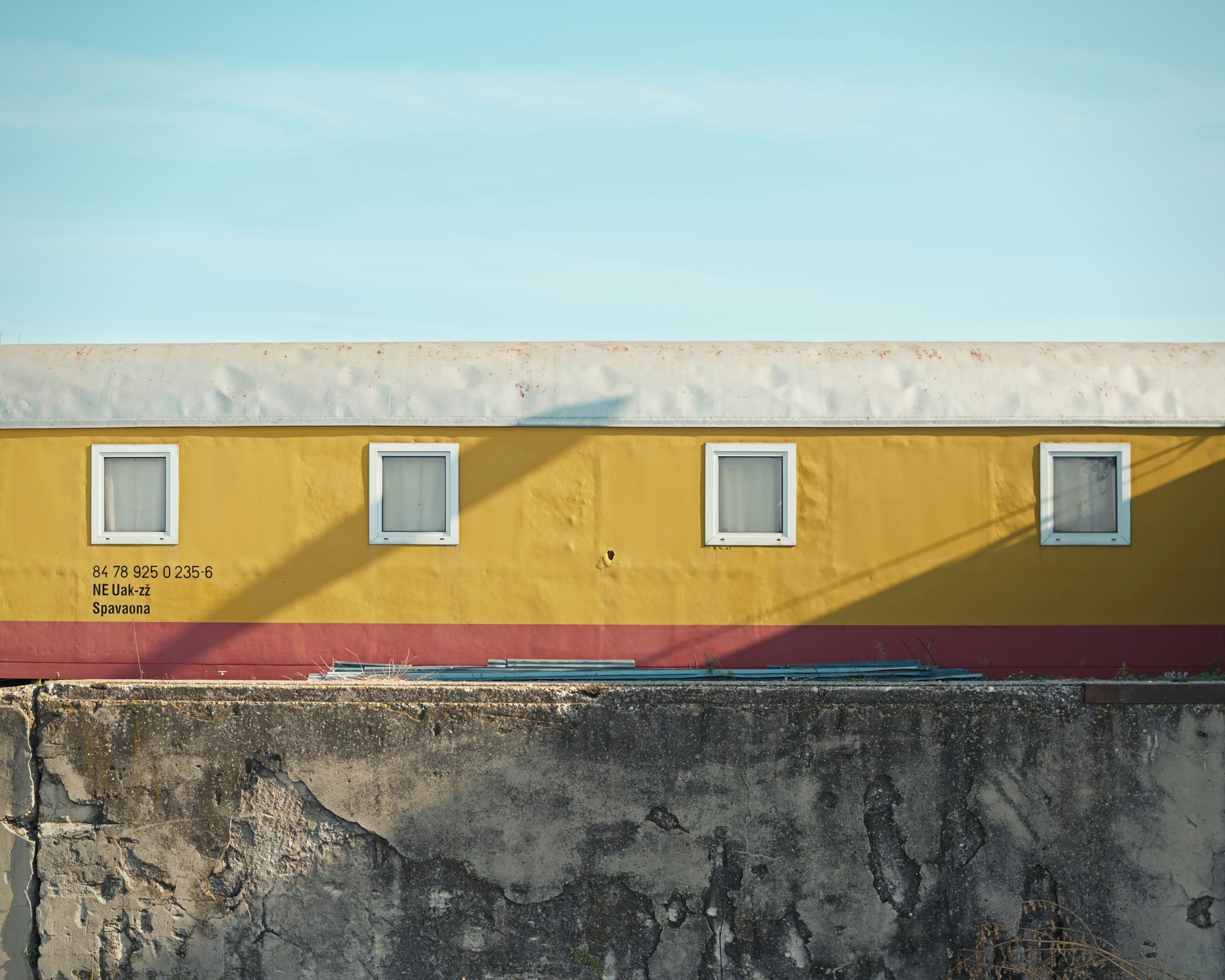 A yellow and red building sitting on top of a cement wall, An abandoned yellow sleeper train in a station behind a concrete wall