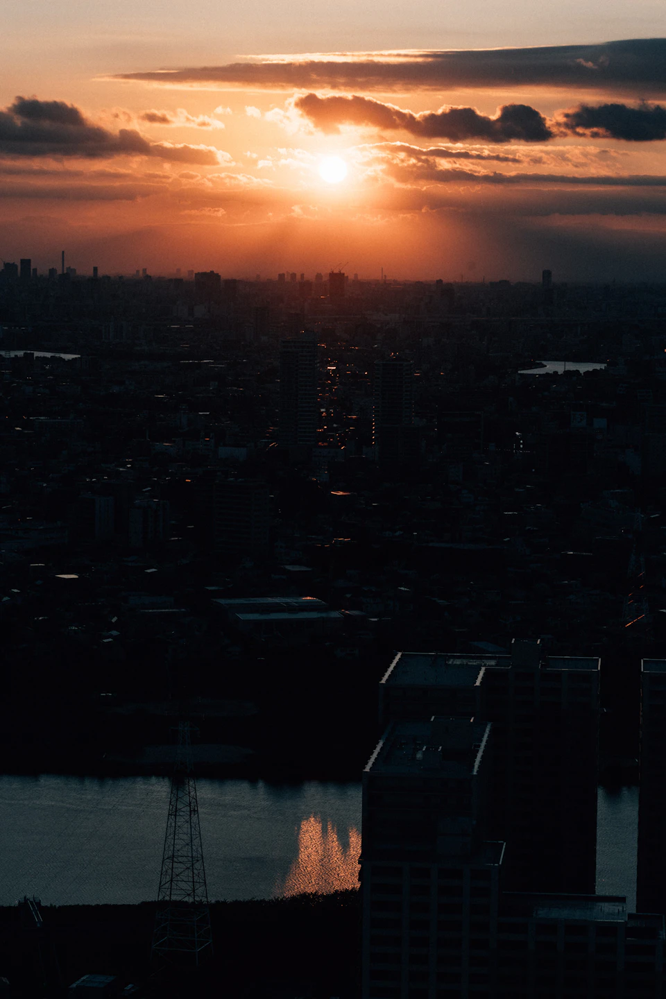 Cityscape at sunset with sun setting behind buildings, casting long shadows across scene