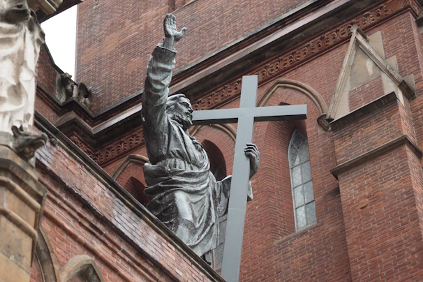 A statue of a person holding a cross in front of a church