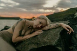 A woman laying on top of a rock next to a body of water