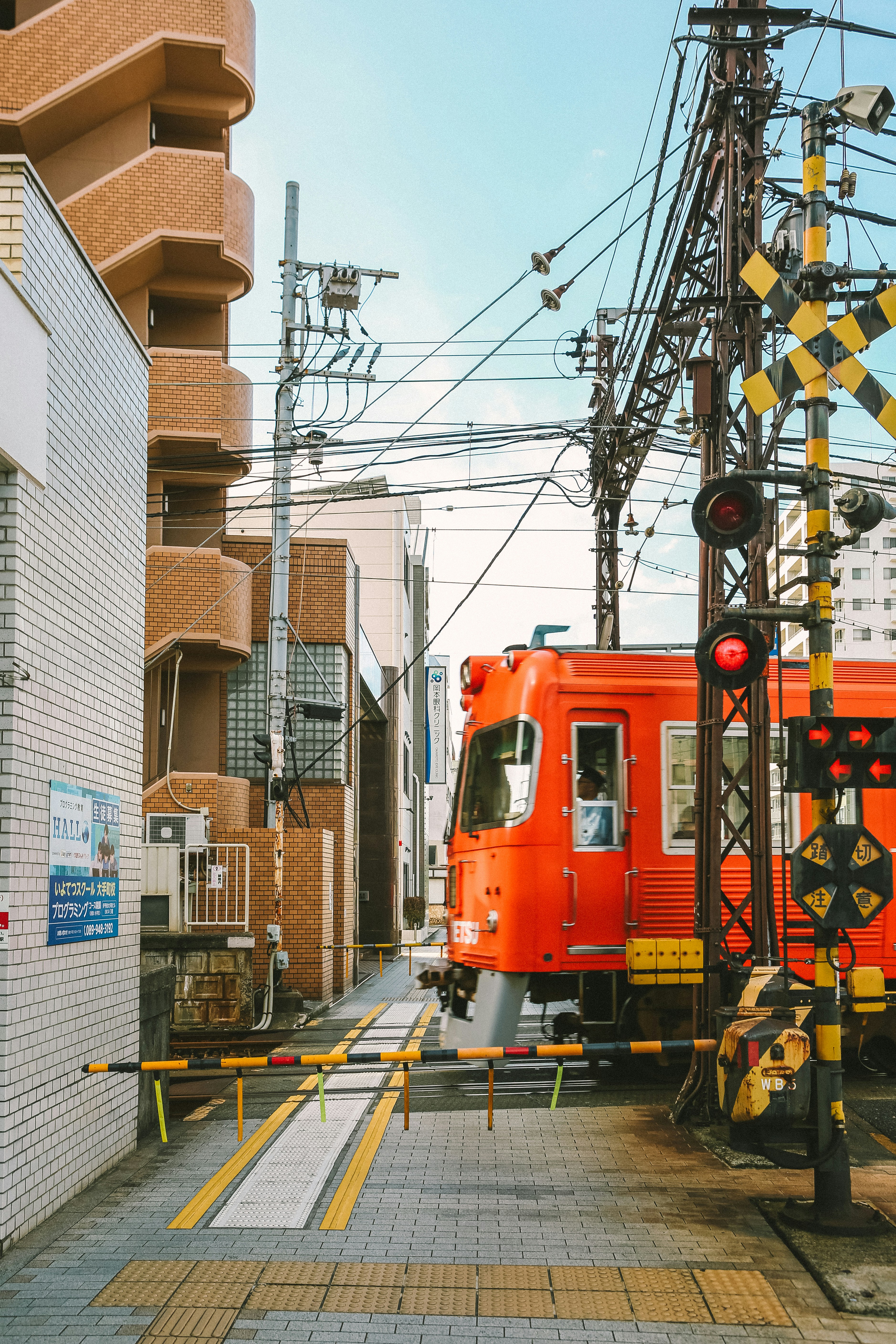 Ein orangefarbener Zug, der neben einem hohen Gebäude die Gleise entlangfährt