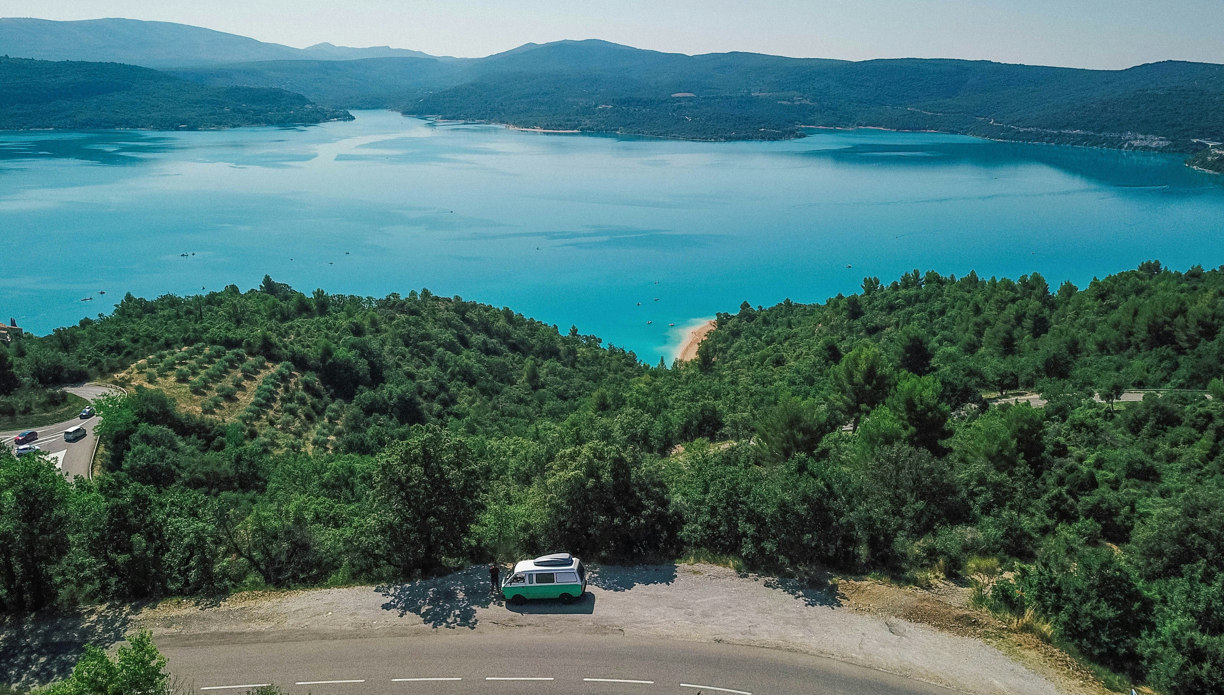 Campervan parked on a winding road overlooking a turquoise lake.