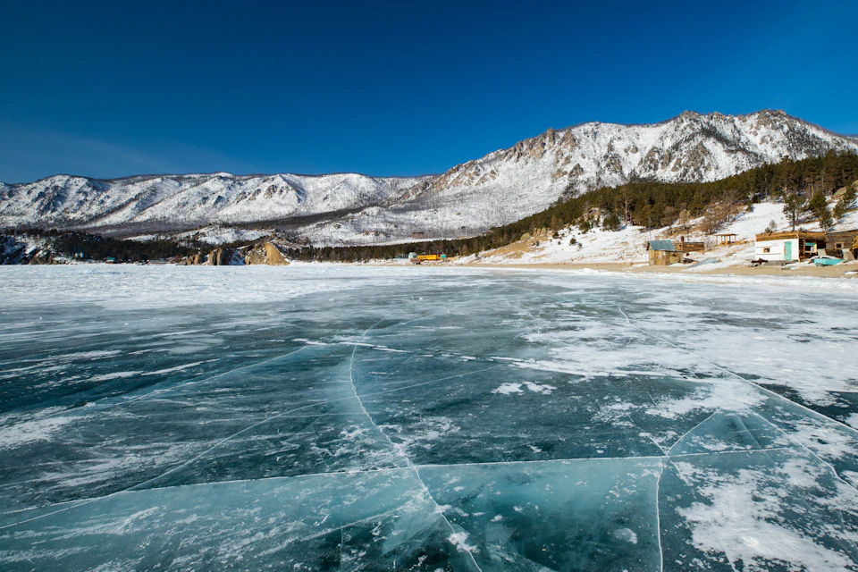 Serene winter landscape with frozen lake surrounded by snow-covered mountains and trees nearby