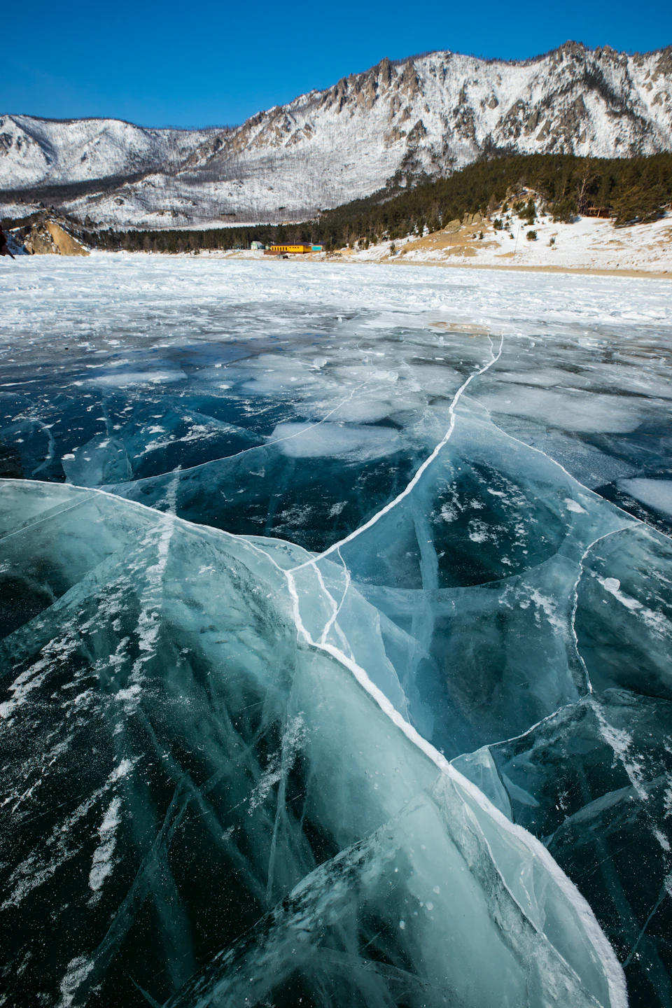 Frozen lake with a central crack in a snowy mountainous landscape under clear blue sky