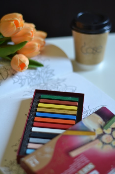 A box of colored pencils next to a cup of coffee