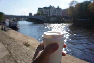 A person holding a cup of coffee near a river