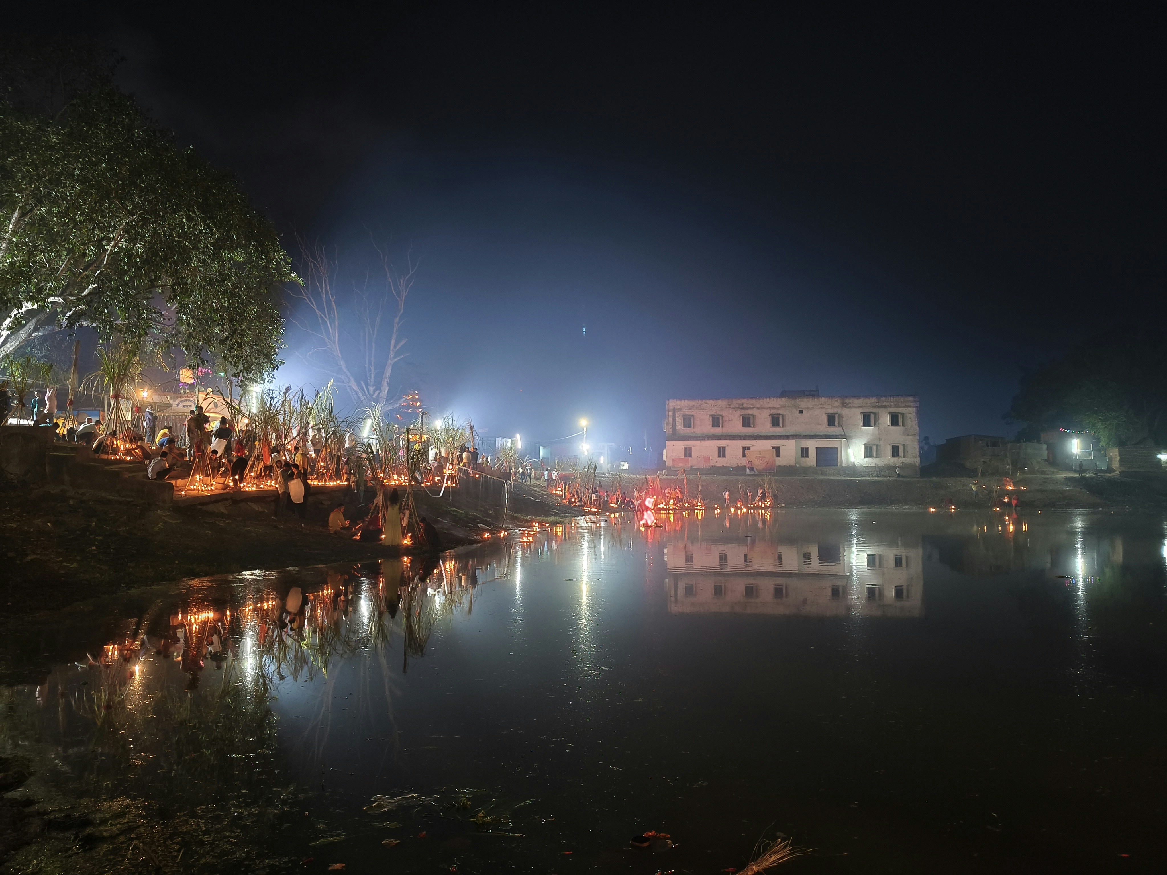 Thousands of devotees gathered at Kumbh Mela at dusk, river glowing with oil lamps, priests performing aarti, smoke and golden light, spiritual atmosphere, dark moody sky