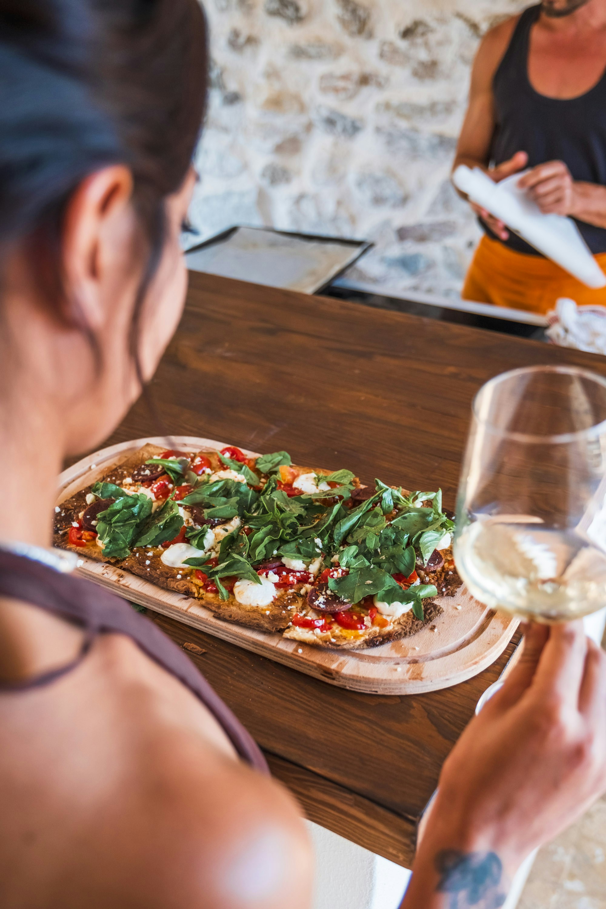 A woman sitting at a table with a pizza and a glass of wine