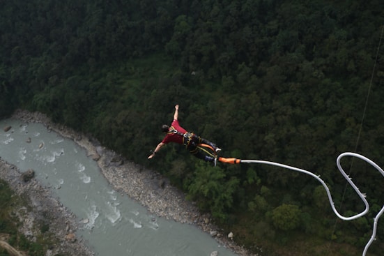 A man is parasailing over a river in the mountains