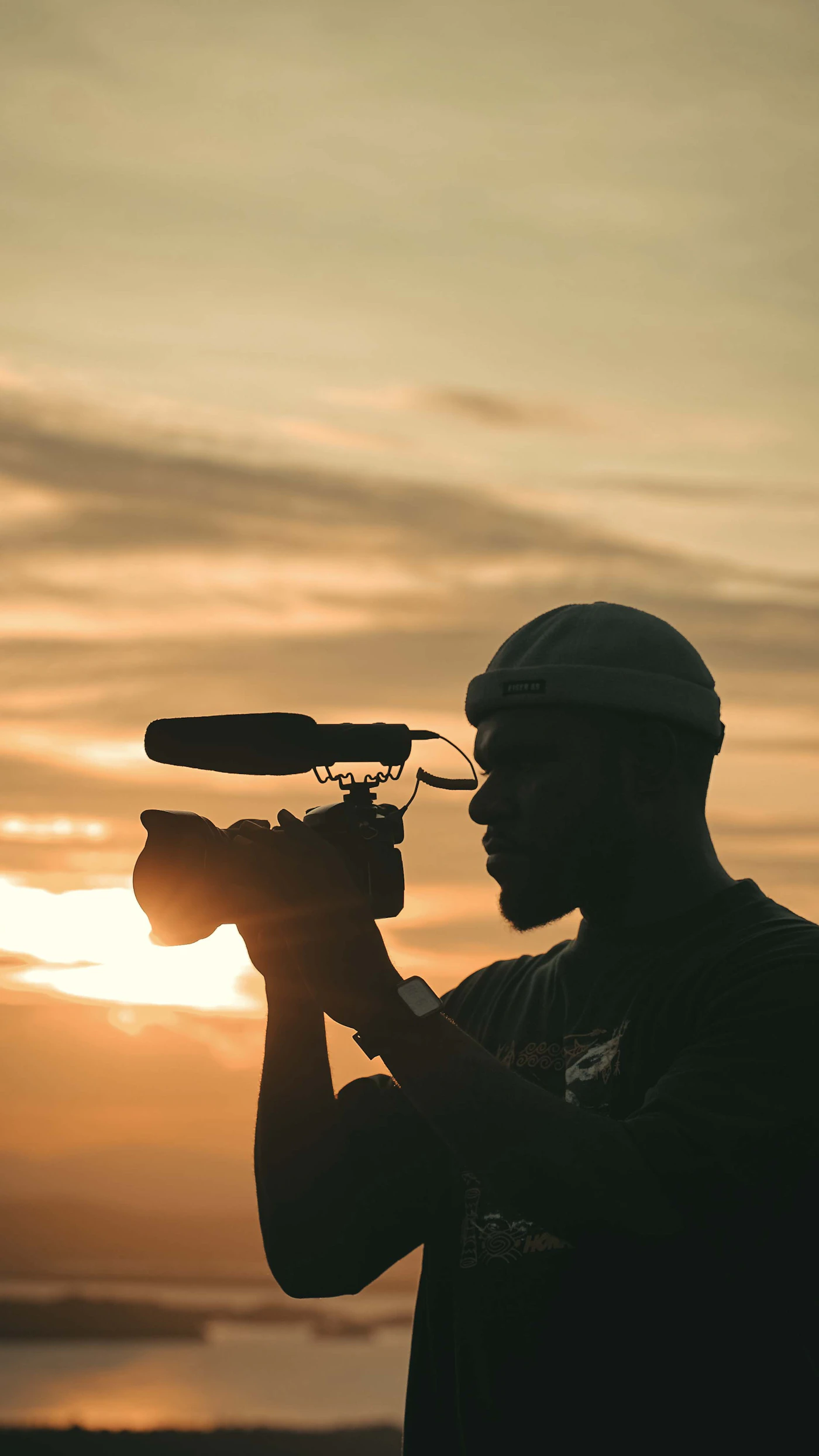 A filmmaker silhouetted against a golden-hour sky, camera raised to shoot