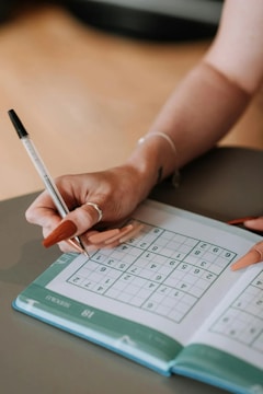 A woman is writing on a crossword puzzle book