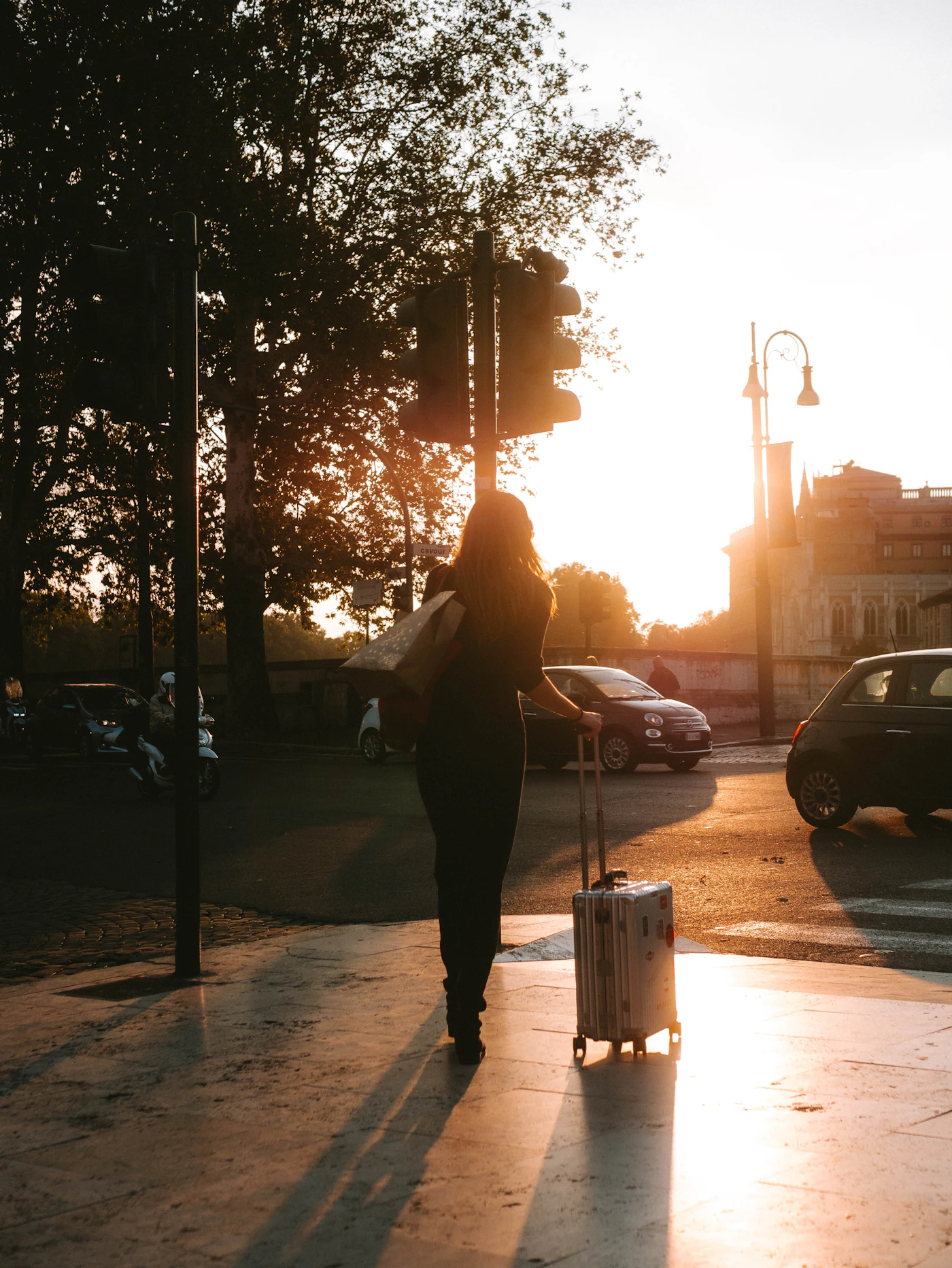 Une voyageuse tire sa valise dans une rue baignée de soleil couchant.
