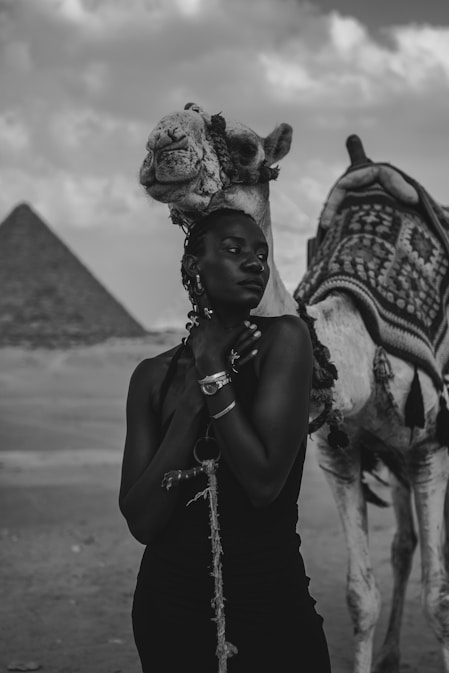 A woman standing next to a camel in front of a pyramid