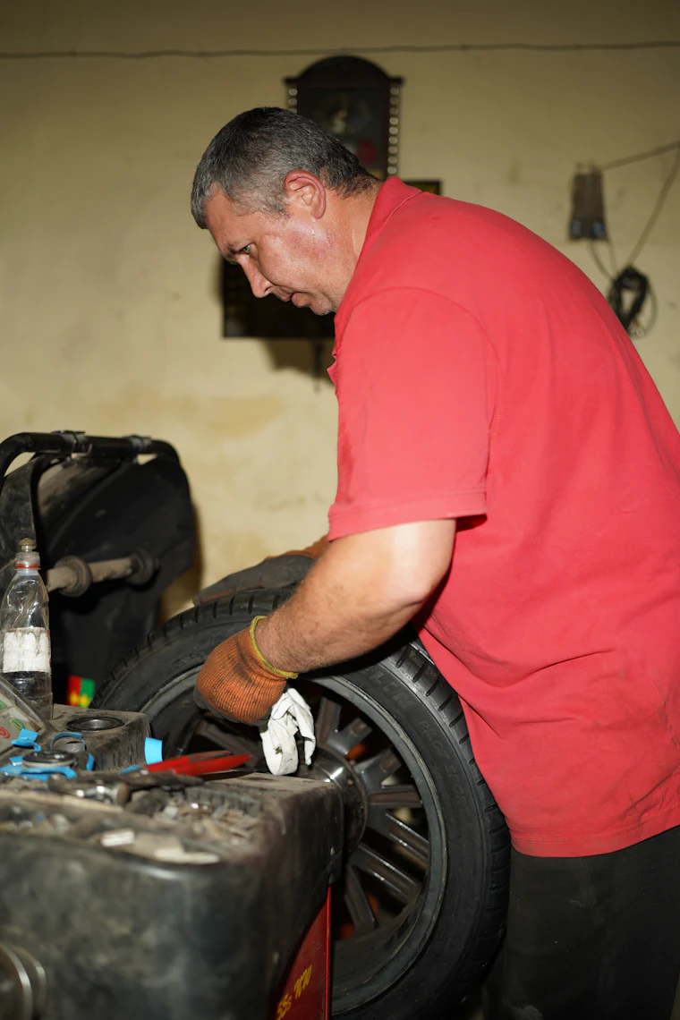 A technician in gloves working a tire onto a wheel rim at a tire machine in a workshop