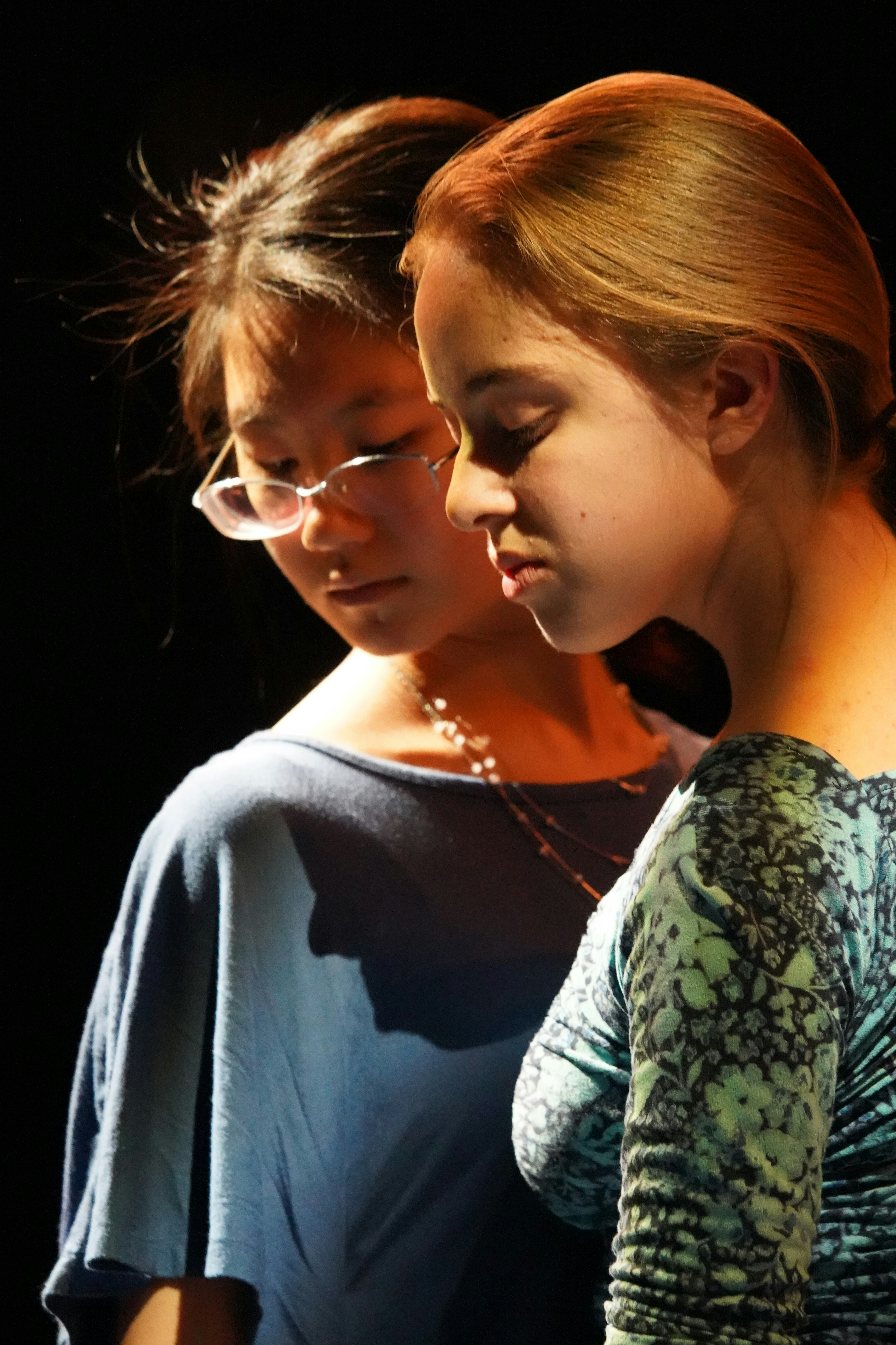 Two women leaning together over one phone, lit by its screen