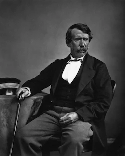 A distinguished man in formal attire sits holding a cane.