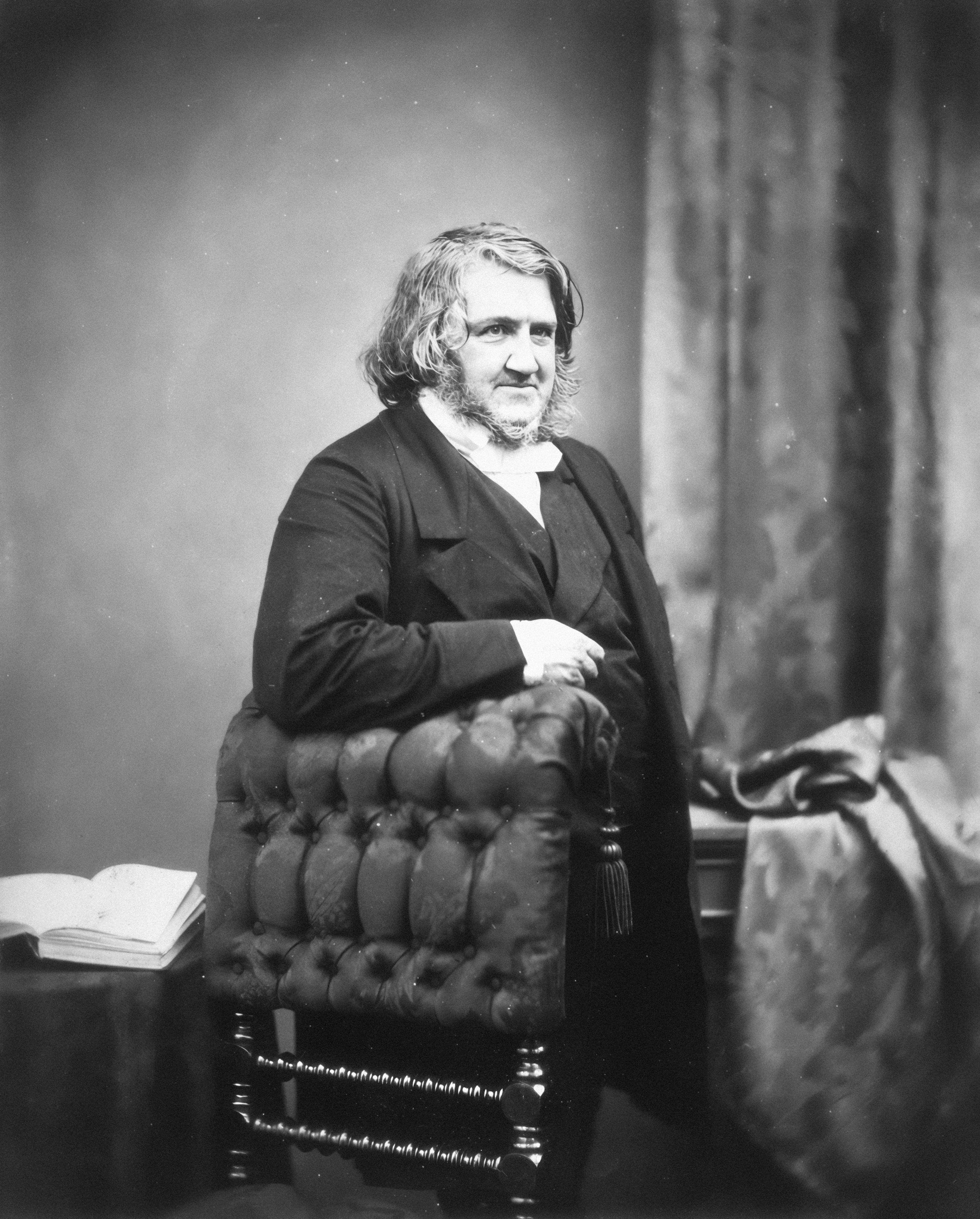 A man in formal attire sits leaning on a chair.