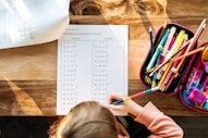 A little girl sitting at a table with a bag of pencils
