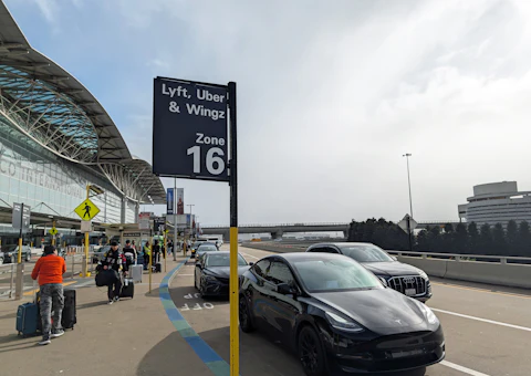 Voyageurs avec valises au bord du trottoir d'un aéroport près d'une voiture, illustrant la prise en charge en taxi à l'aéroport de Casablanca
