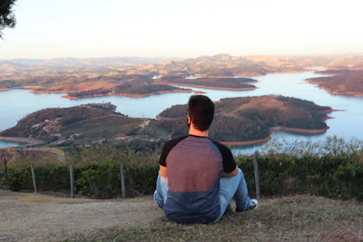 A man sitting on top of a hill overlooking a lake