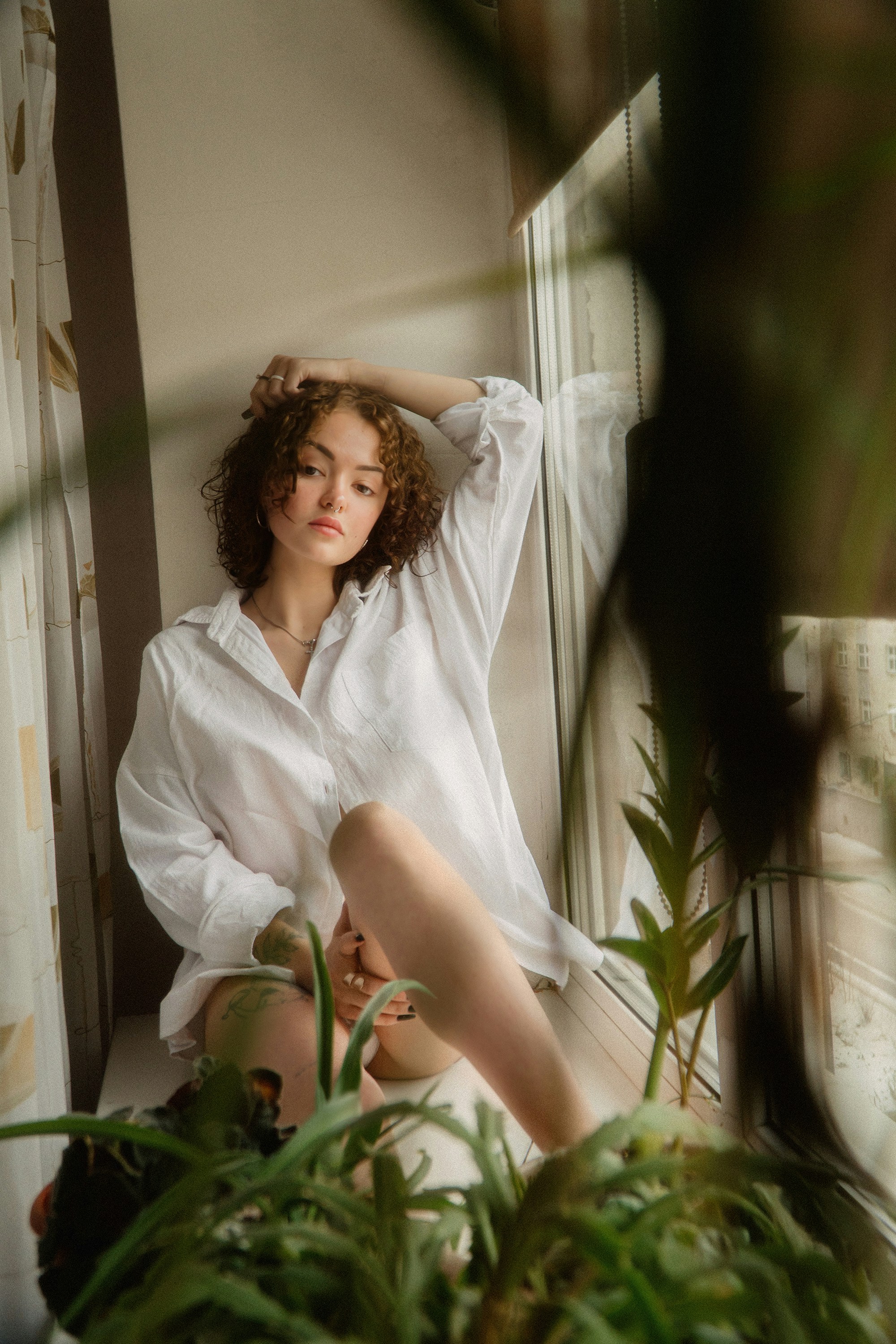 A woman sitting on a window sill next to a plant