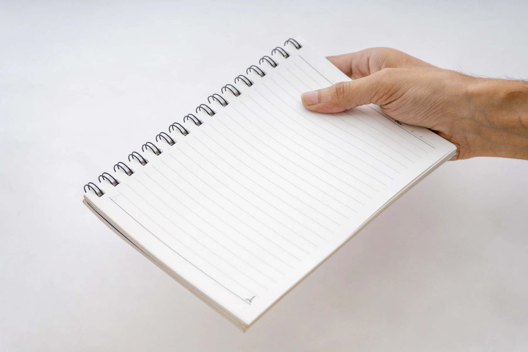 A hand holding out a ruled notebook bound with a wire spiral along its top edge