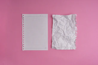A pink wall with a notepad and a pair of scissors