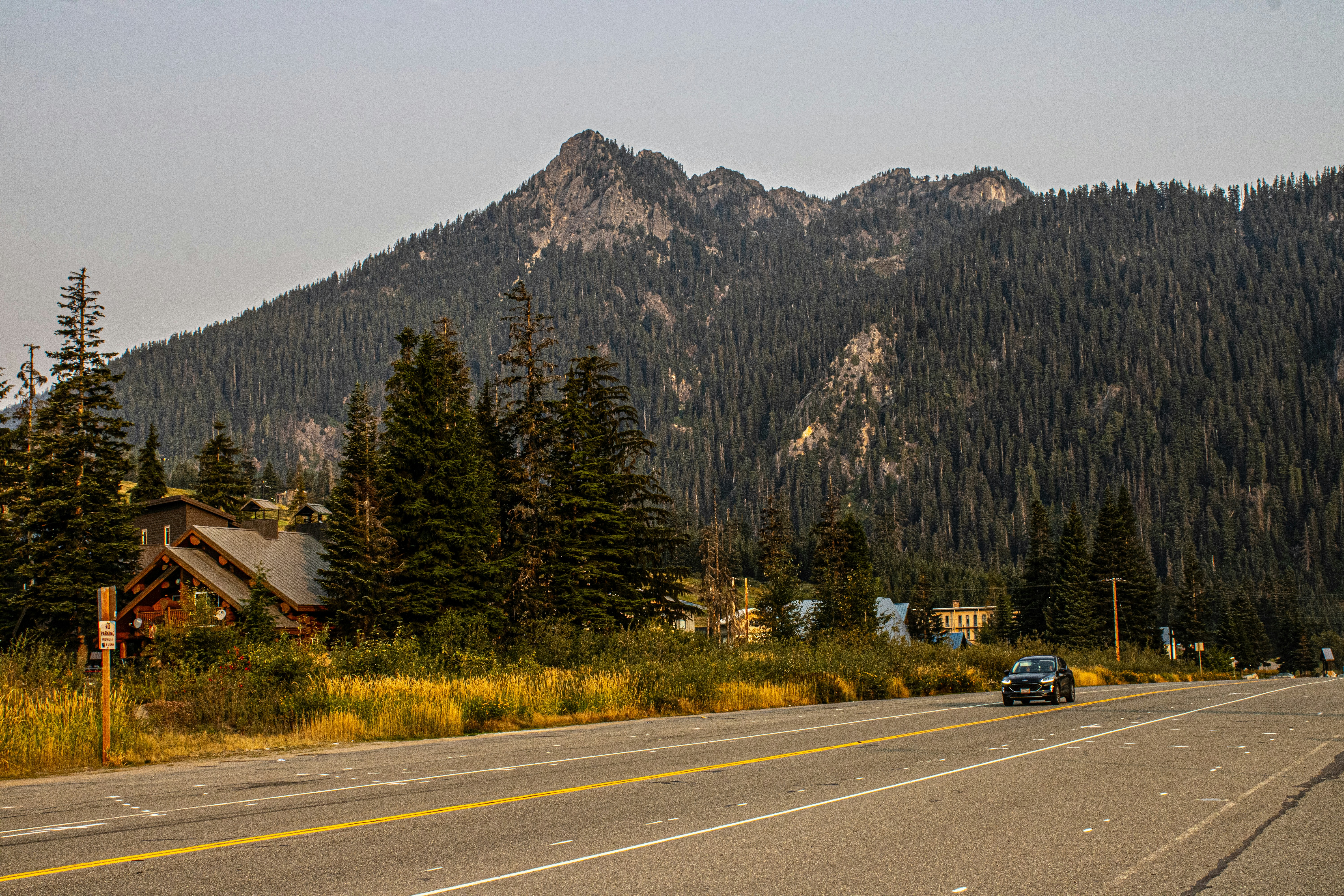 A car is driving down a road in front of a mountain