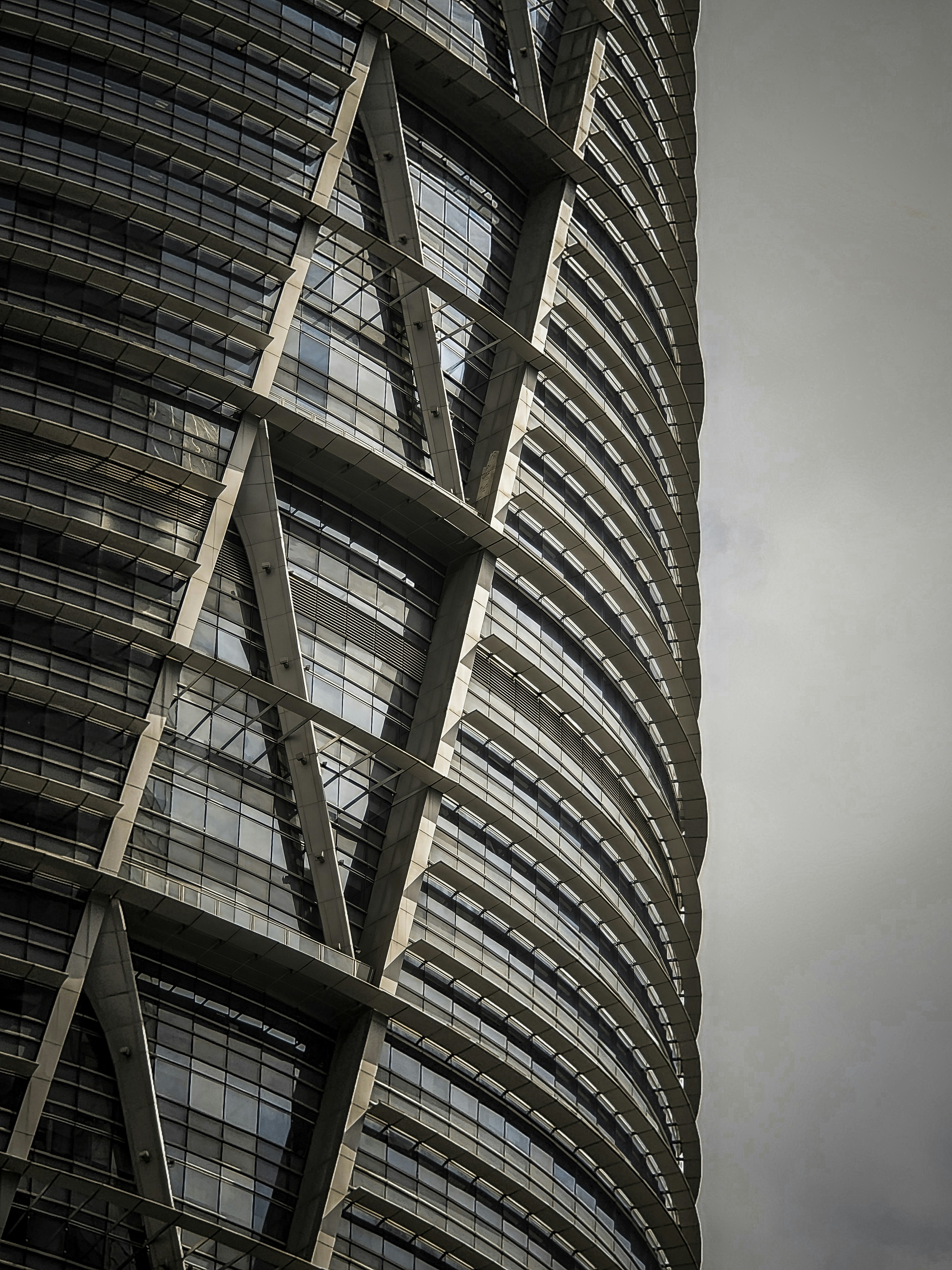 Glass commercial tower with angular facade, grey overcast sky, deep shadows on steel panels, low-key urban atmosphere