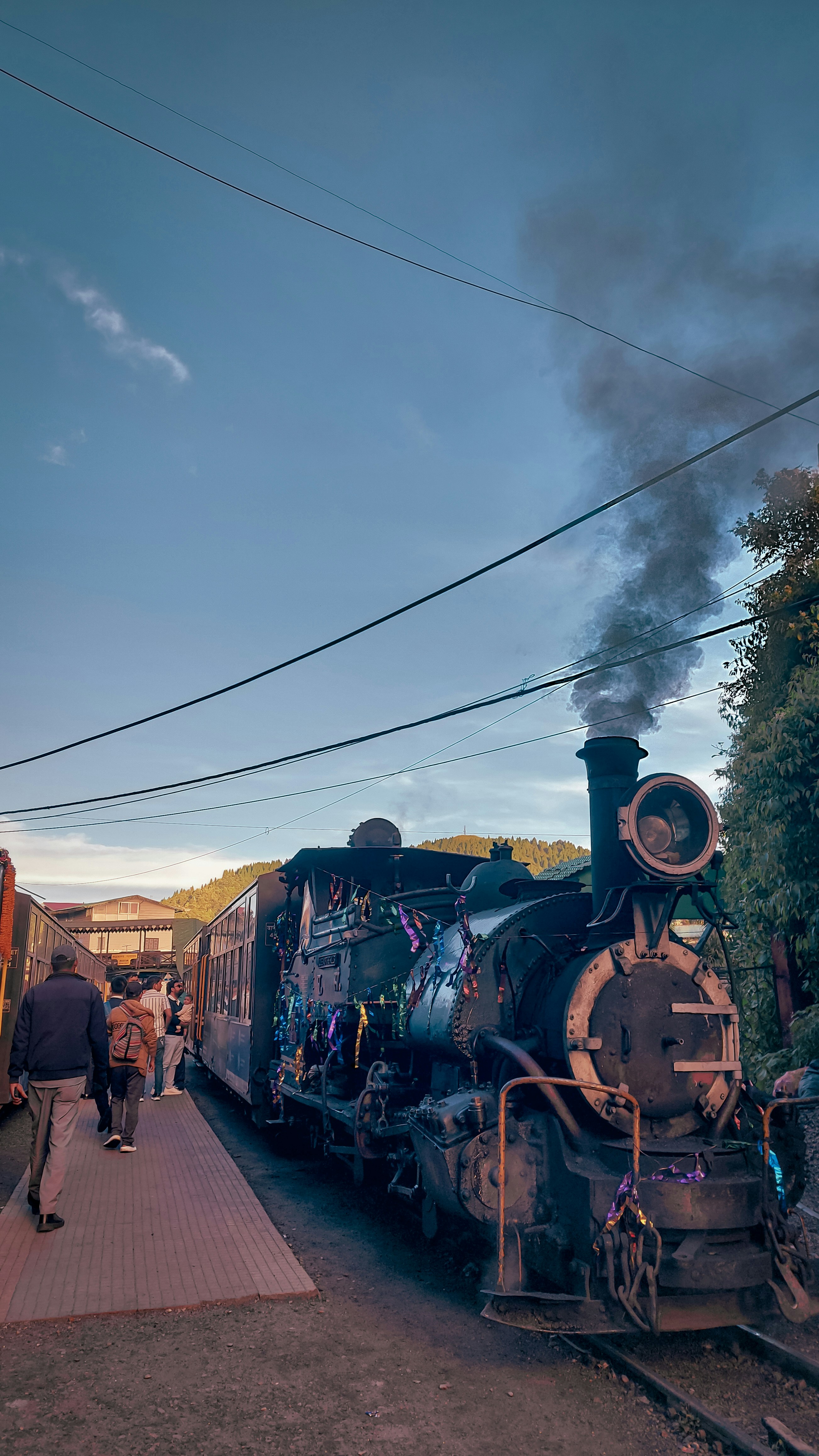 Heritage steam locomotive departing grand Victorian station at dusk, golden platform lights illuminating billowing steam clouds and elegantly dressed passengers