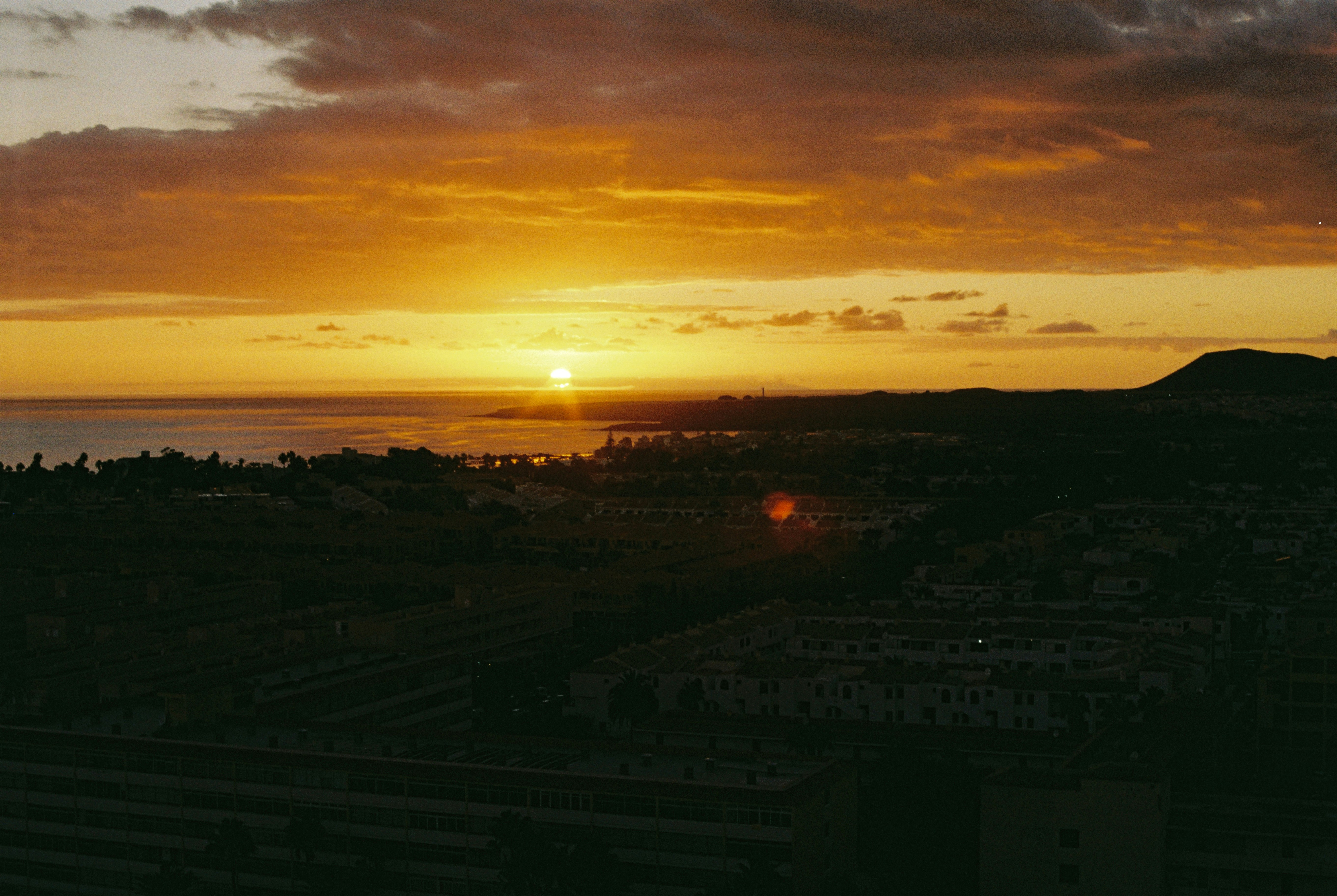 The sun is setting over the ocean and a city