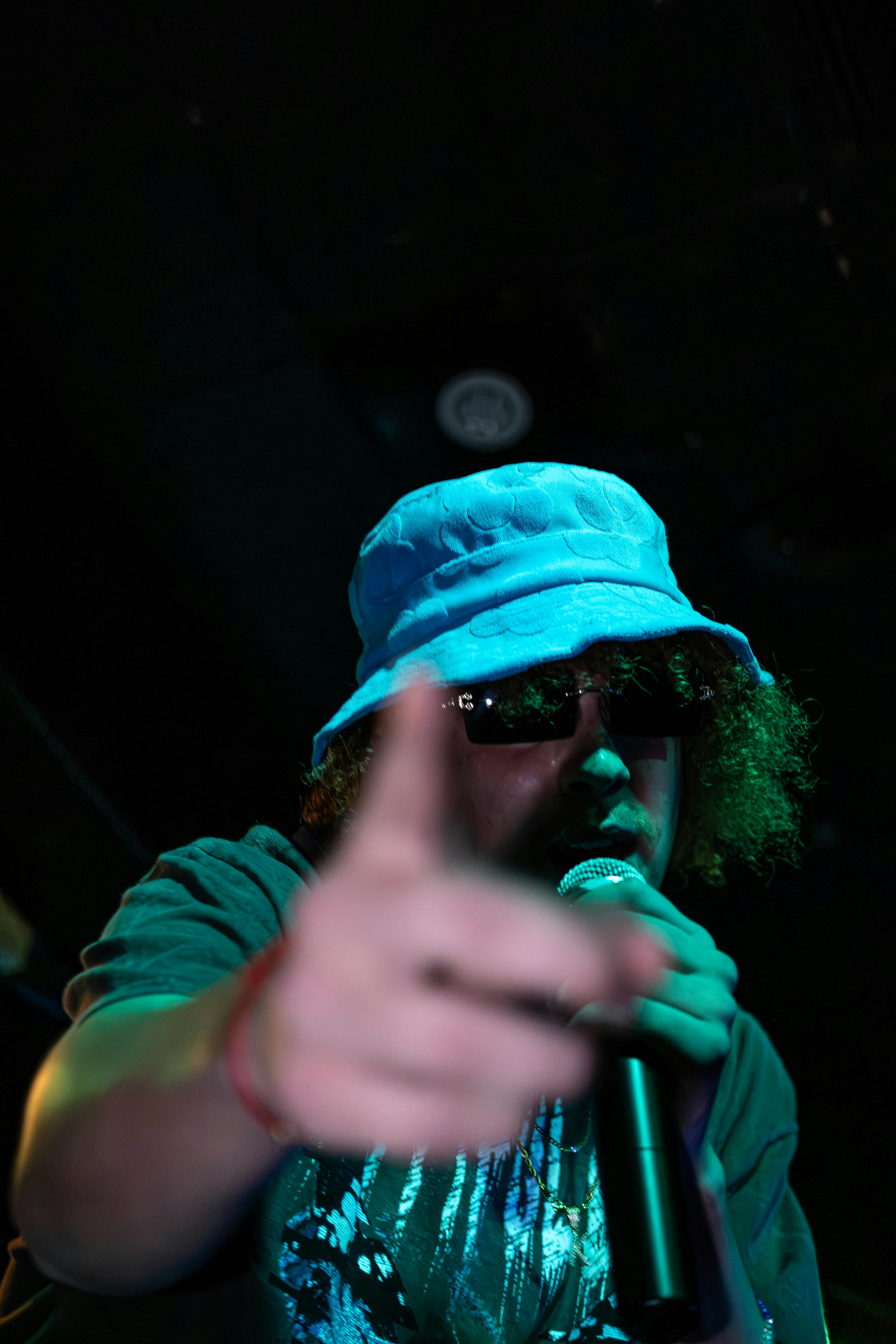 Ein Mann mit blauem Hut und Sonnenbrille hält ein Mikrofon in der Hand