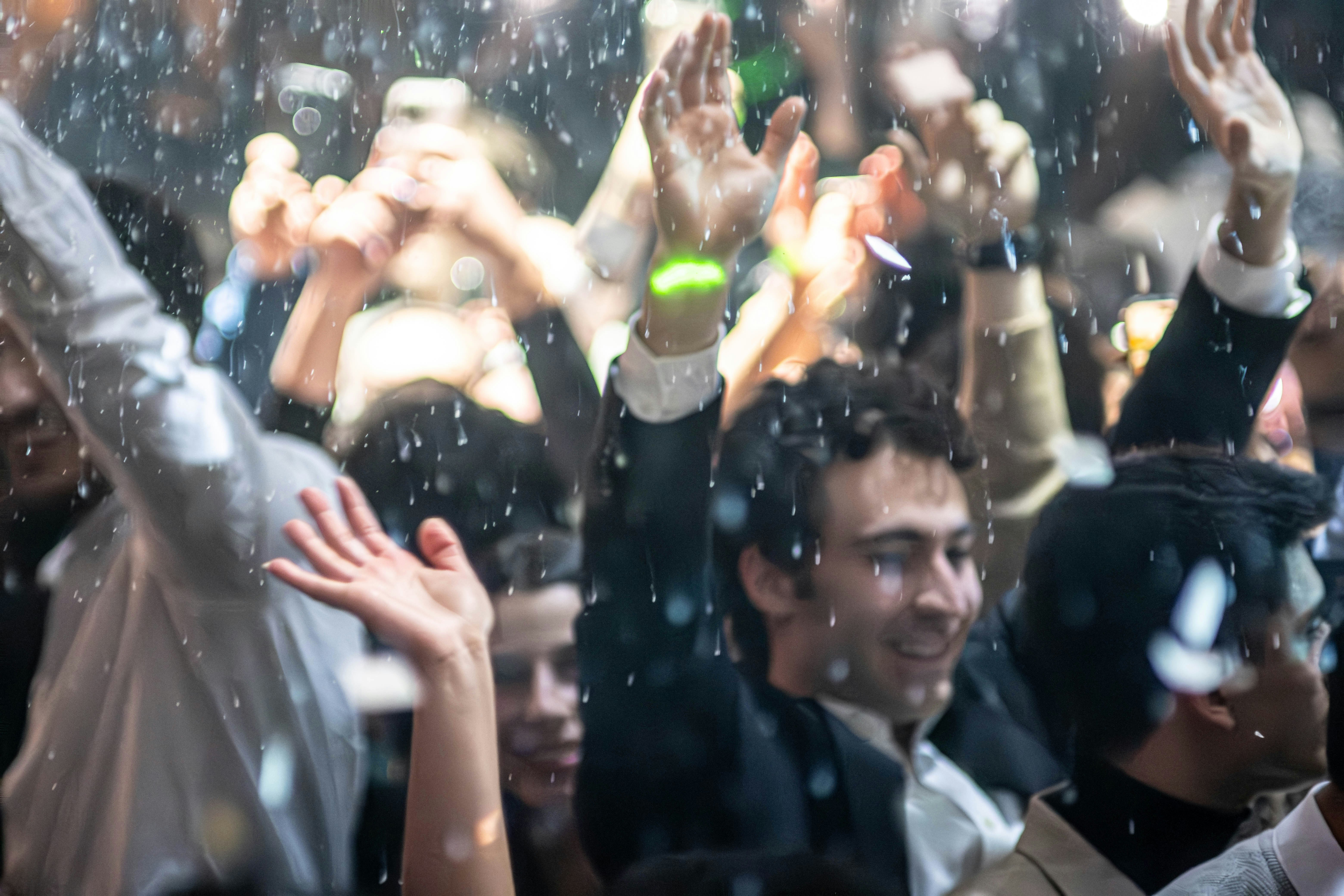 Party celebration with colourful lights and confetti, crowd dancing with raised hands