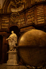 A statue of a man in a library next to a globe