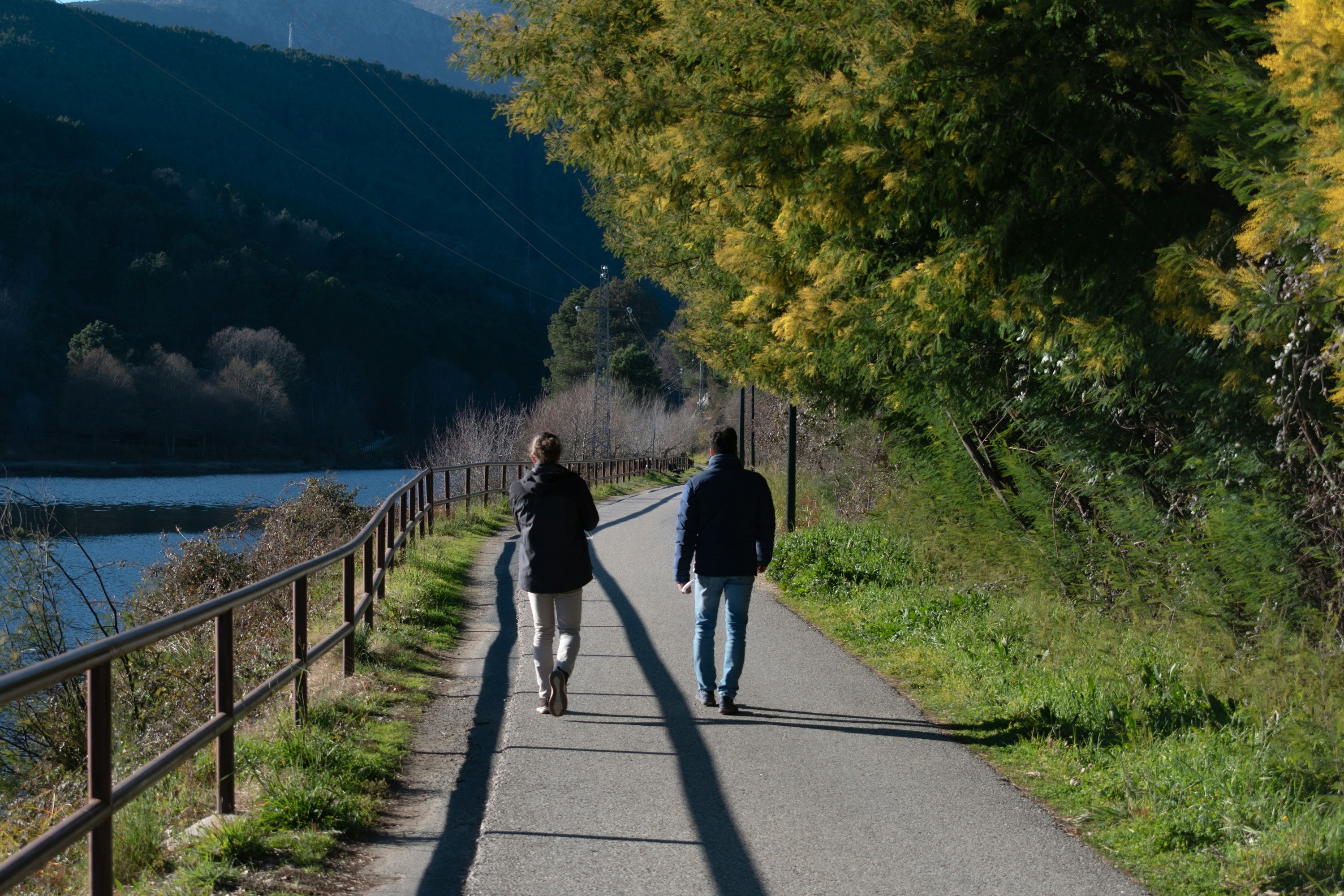 A couple of people walking down a road next to a lake