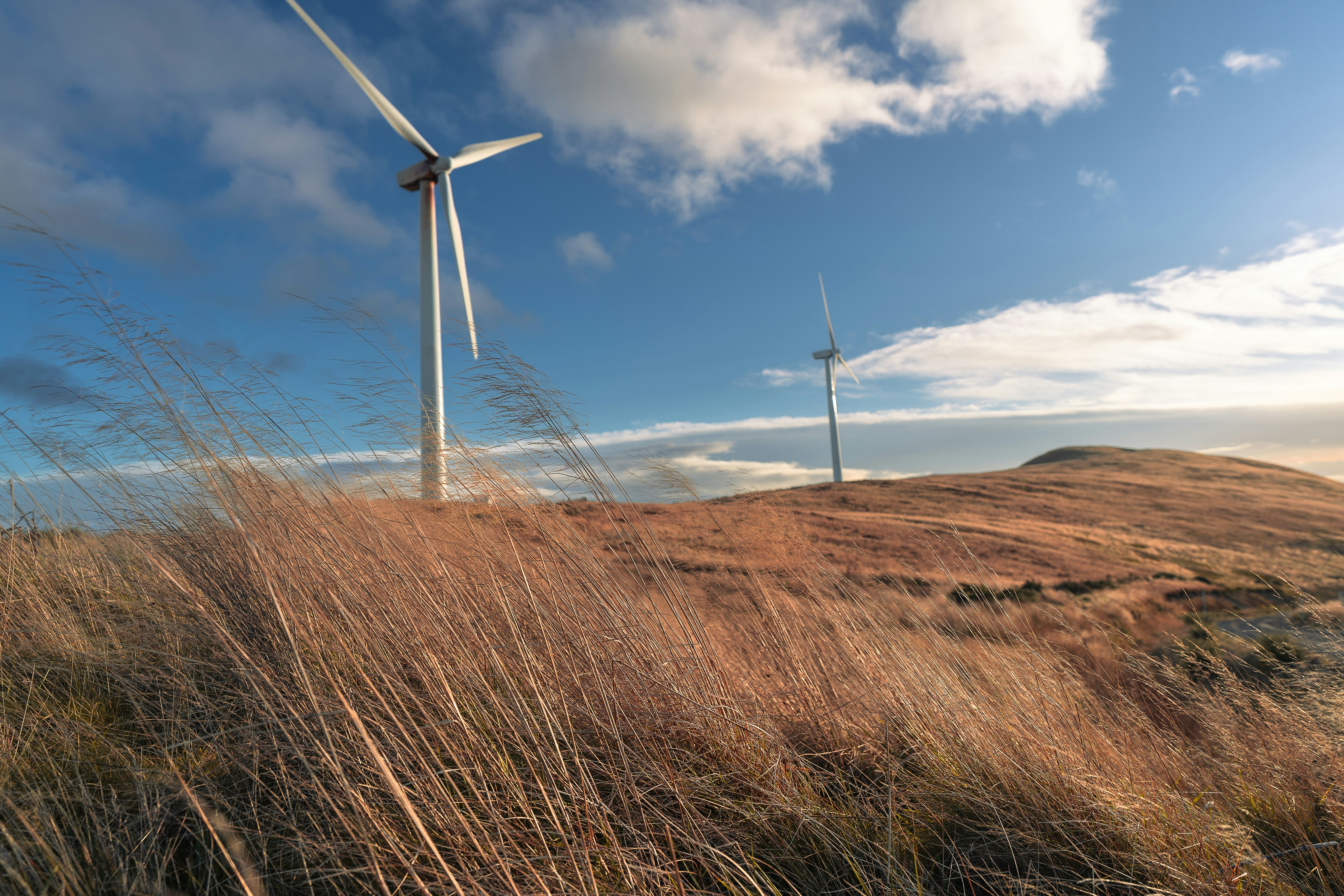Three wind turbines on a grassy hill under a blue sky