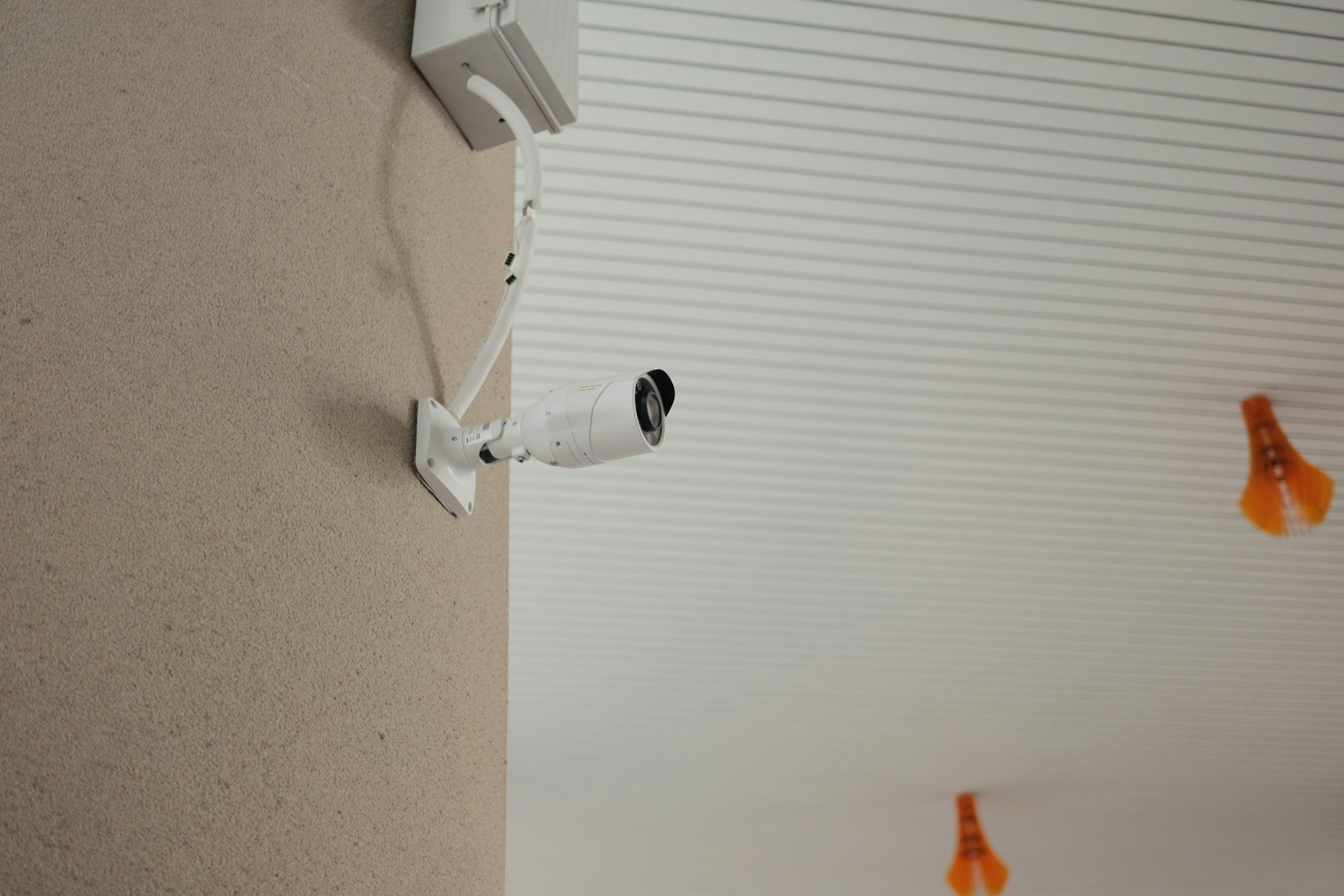 CCTV security camera mounted on white ceiling in bright institutional corridor