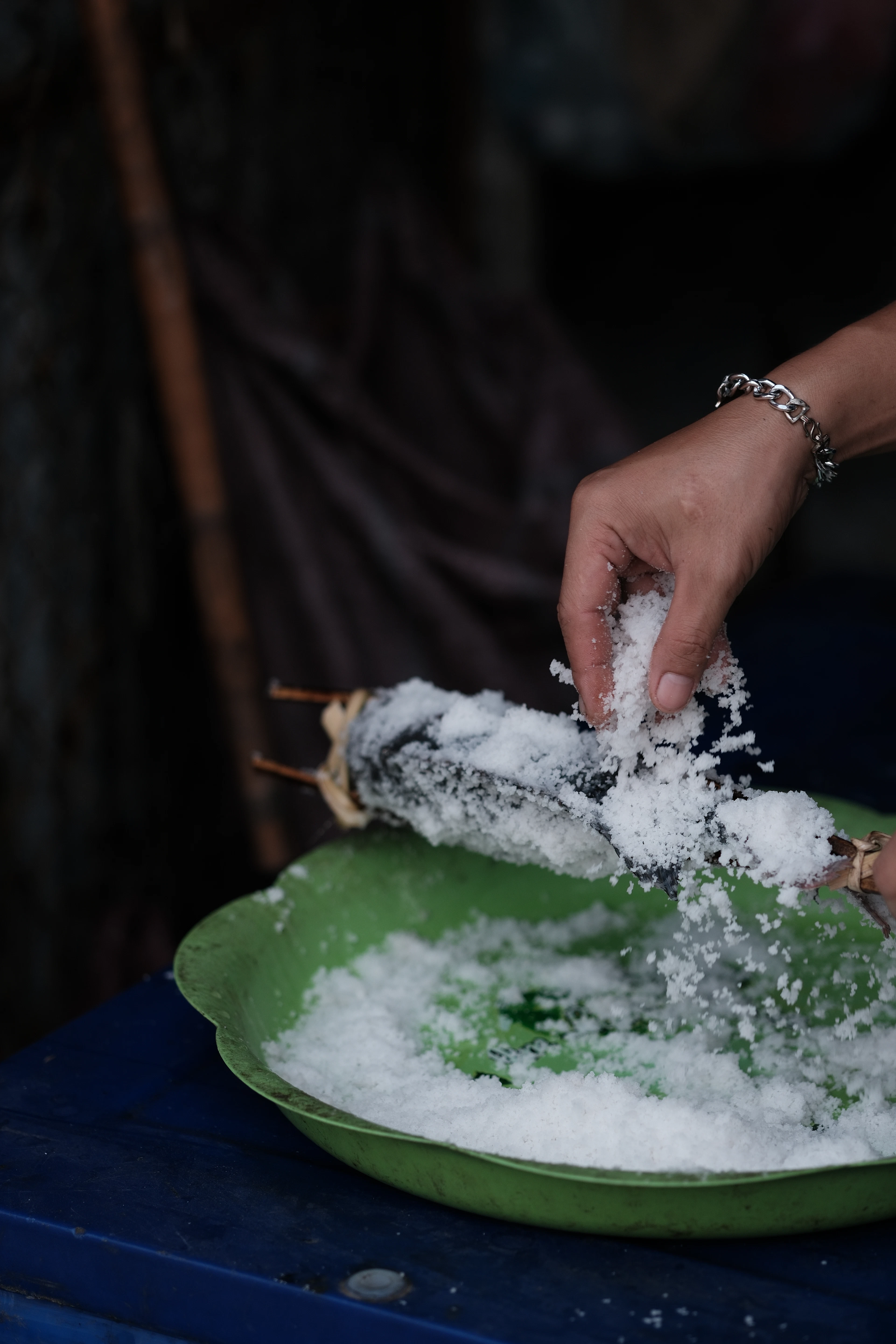 Hands packing coarse salt onto a whole fish before it is grilled, at a food stall in Luang Prabang, Laos