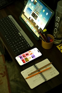 A desk with a laptop, keyboard, phone and a cup of pencils