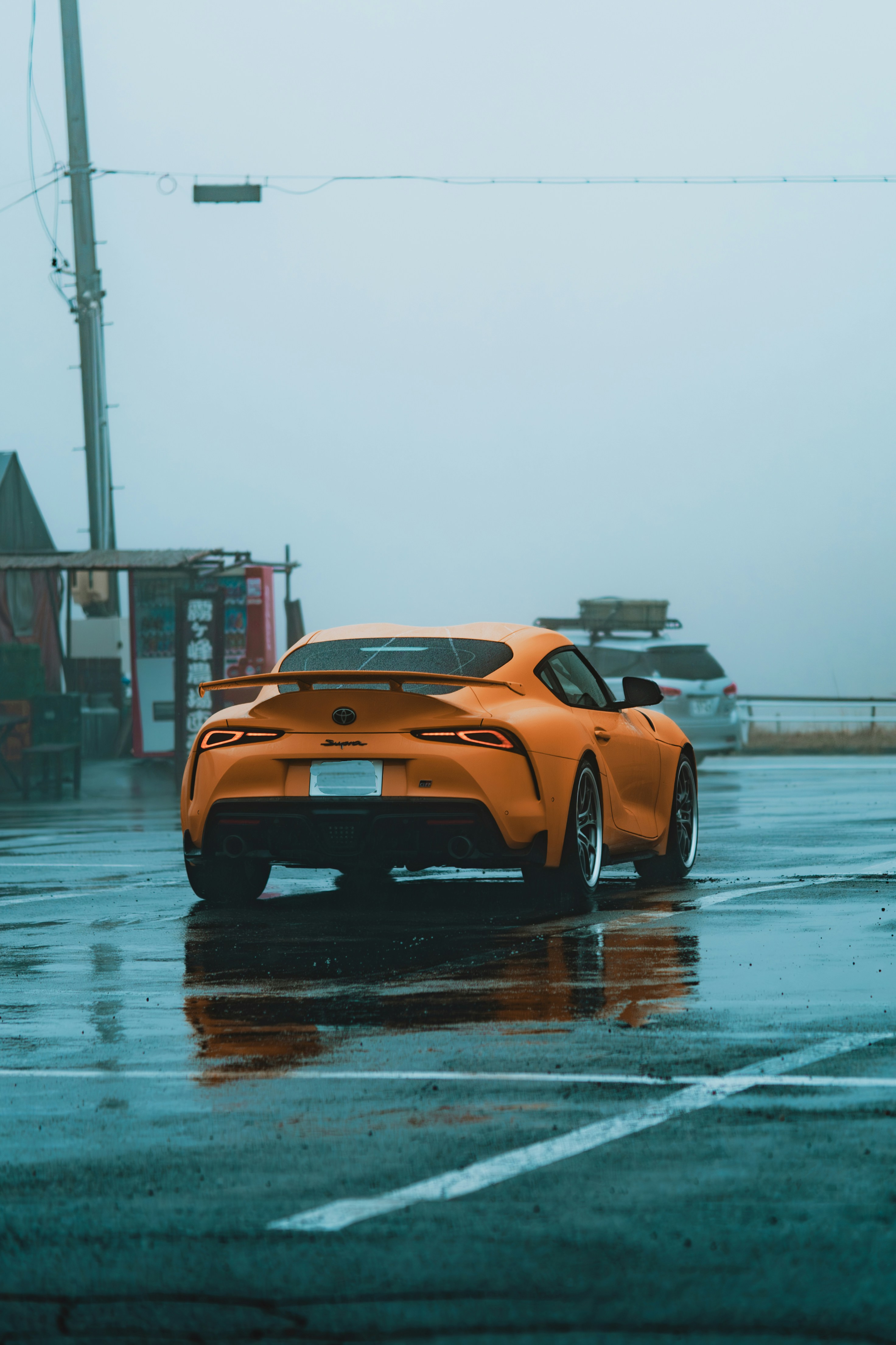 An orange sports car driving down a wet road