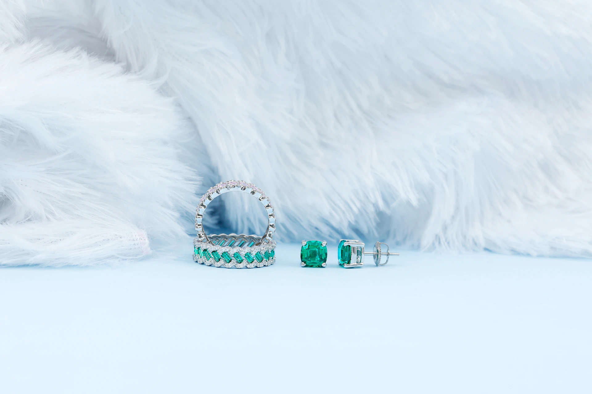 A pair of emerald earrings sitting on top of a white fur