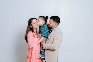 A man and a woman holding a baby in front of a white wall