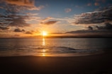 The sun is setting over the water on the beach