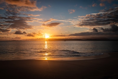 The sun is setting over the water on the beach