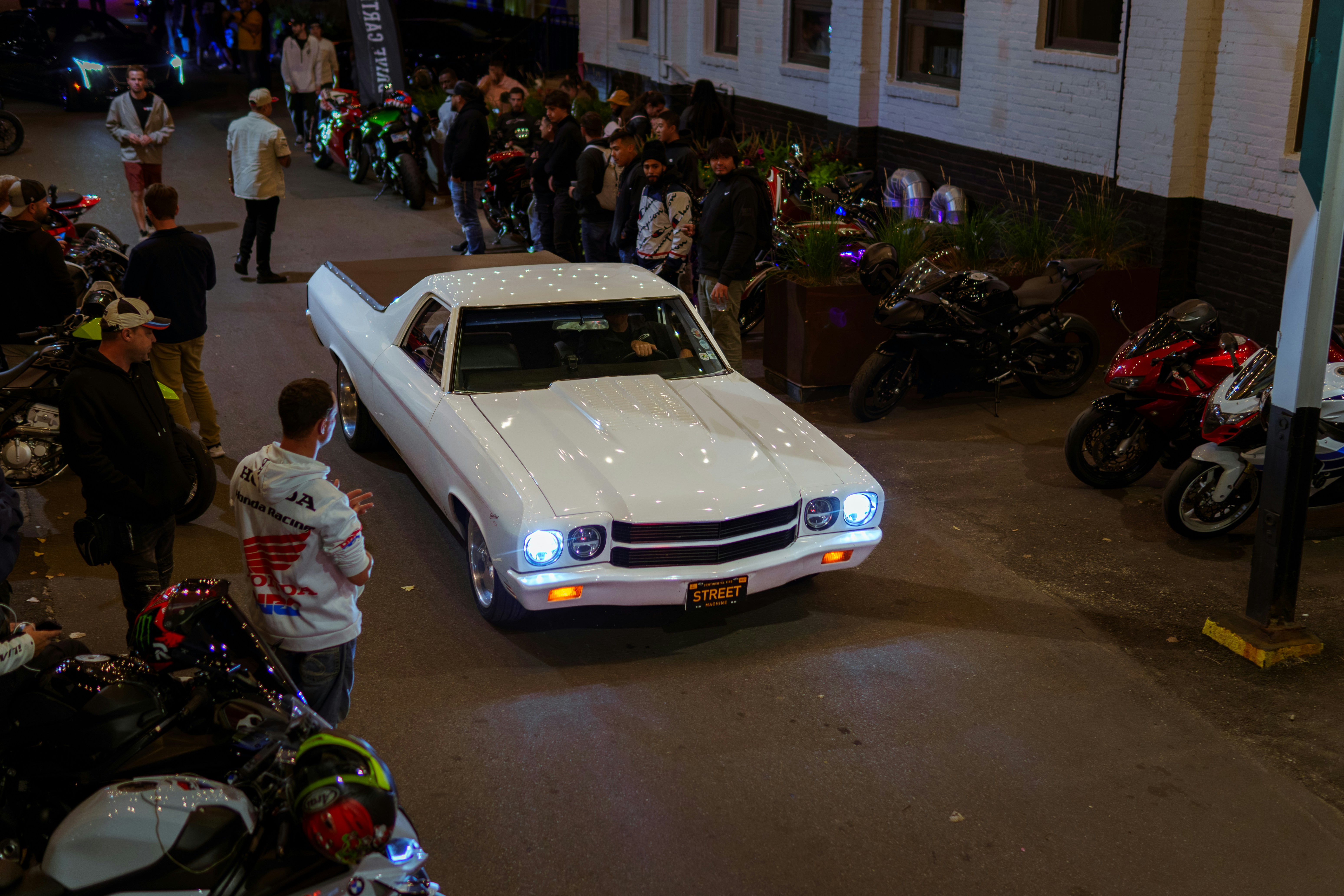 A white car driving down a street next to a crowd of people photo ...