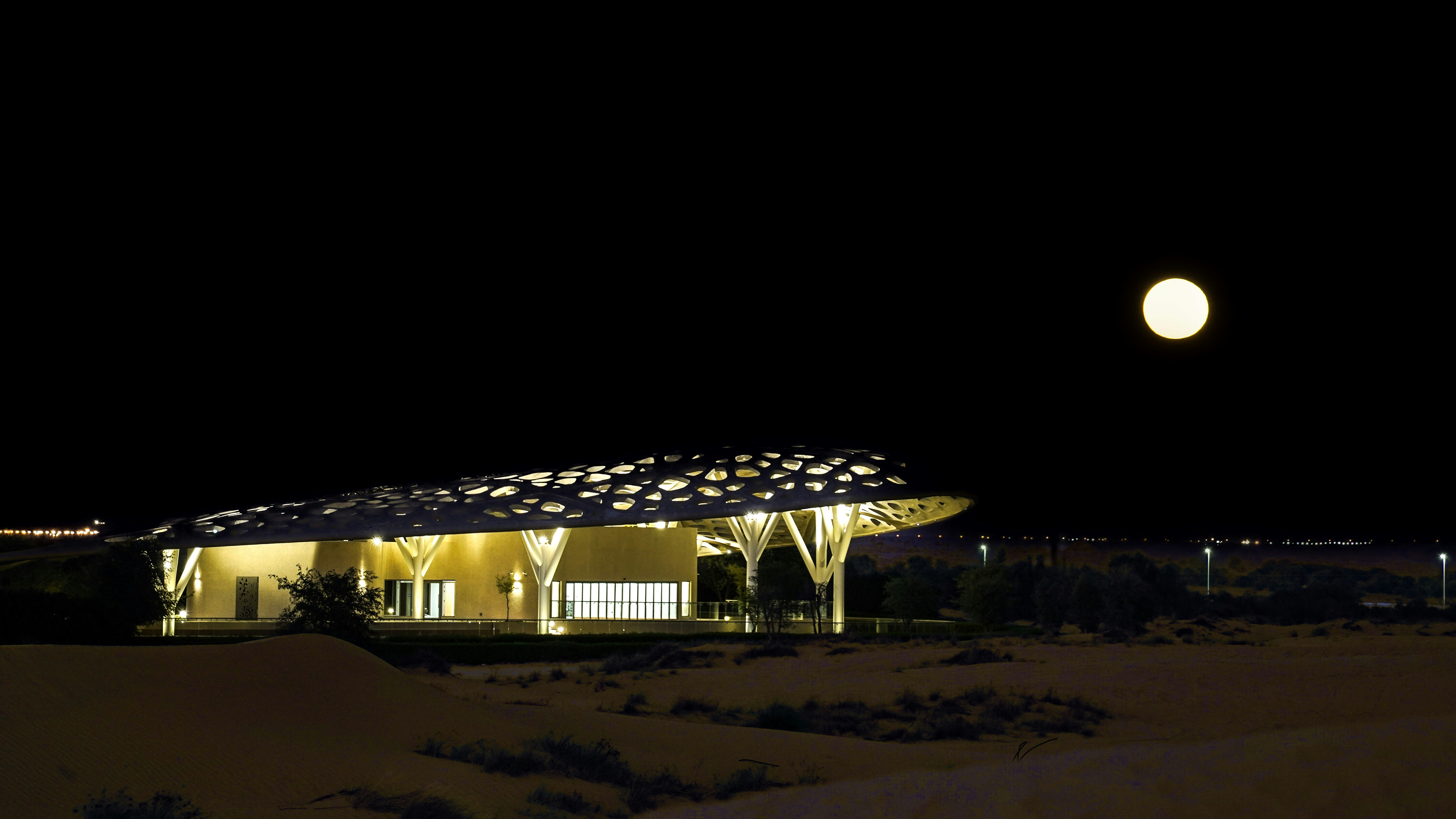 A building lit up at night with a full moon in the background