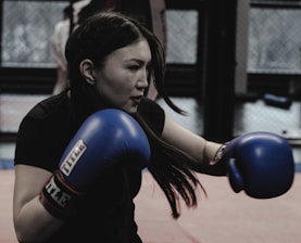 A woman in a black shirt and blue boxing gloves
